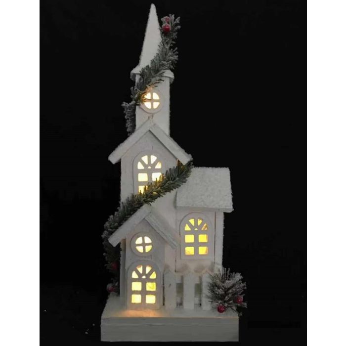 Tall white lighted Christmas chapel with glowing windows, snowy roof and evergreen accents