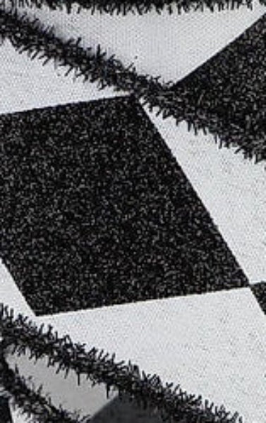 Black and white harlequin patterned ribbon with a fringed edge, wound on a white spool against a white background.
