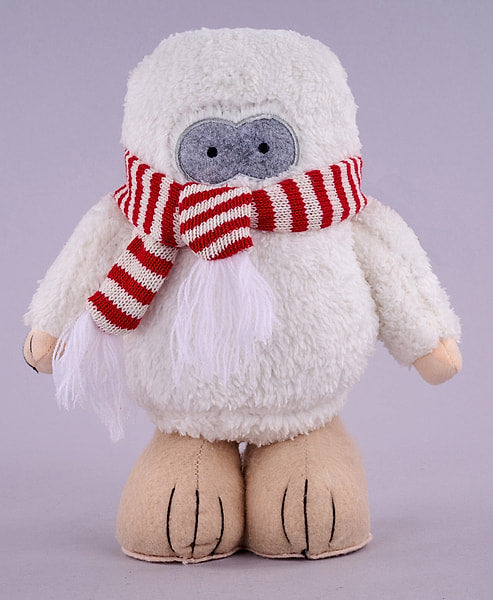 A plush toy of a white furry character with a red and white striped knit scarf, a gray fabric face, and tan feet, set against a solid light purple background.
